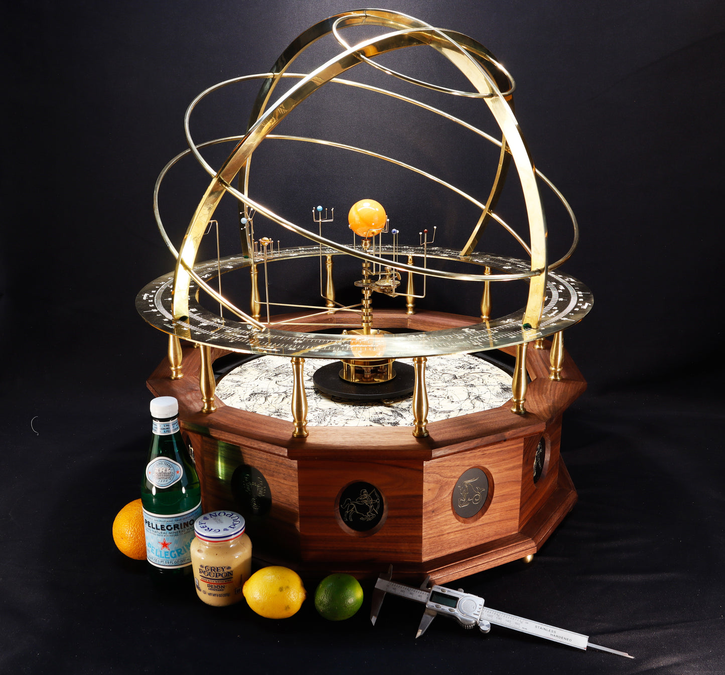 A premium museum, gallery quality, grand orrery with a solid brass calendar ring, brass planets and moons, and a half armillary sphere on top, all mounted on a hand-oiled black walnut wood base. Twelve panel depict each sign of the zodiac. Depicted here along side a lemon and lime, mustard jar to denote the size of the two foot diameter
