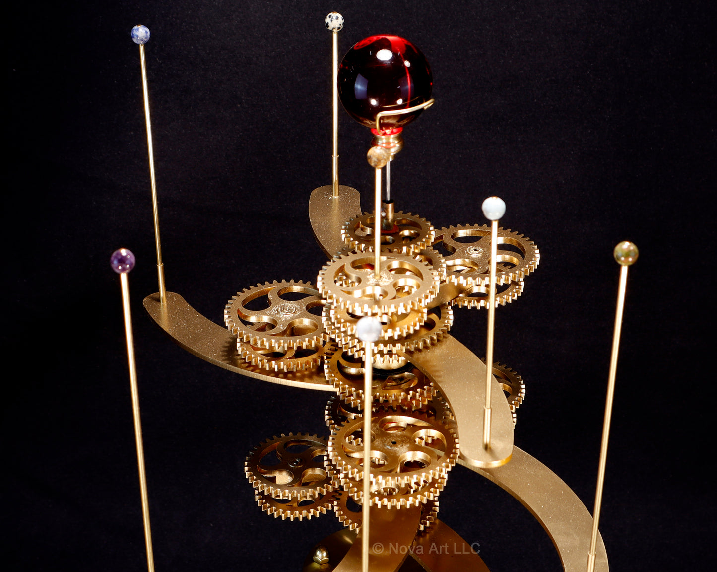 The brass gearworks of the Trappist-1 solar system orrery, the gears drive the semi-precious stone planets around dwarf sun depicted in a sphere of red glass.