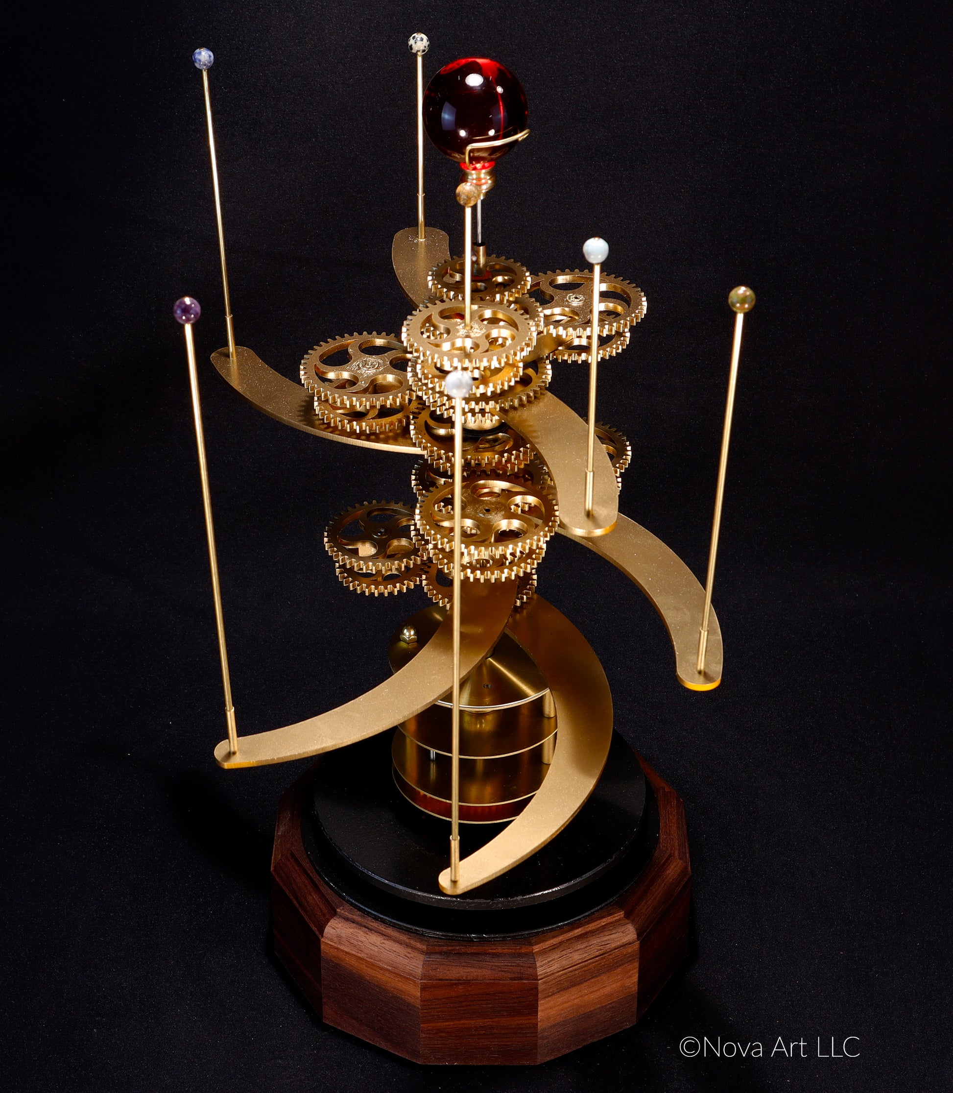The brass gearworks of the Trappist-1 solar system orrery, the gears drive the semi-precious stone planets around dwarf sun depicted in a sphere of red glass.