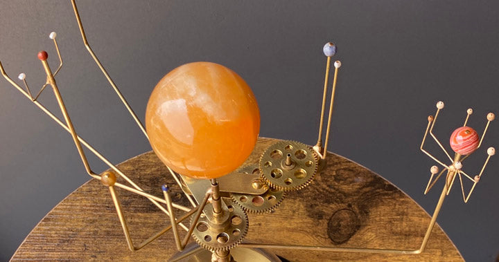 Close up of the Semi-precious planets and orange calcite Sun of the pedestal table orrery and the brass earth moon system gearing.