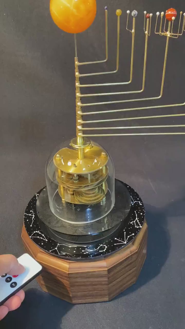 Video demonstrating the remote control on off operation of a solar powered orrery model featuring a glass dome, brass gears, semi-precious stone planets in orbit around an orange calcite sun, mounted on a hardwood base.