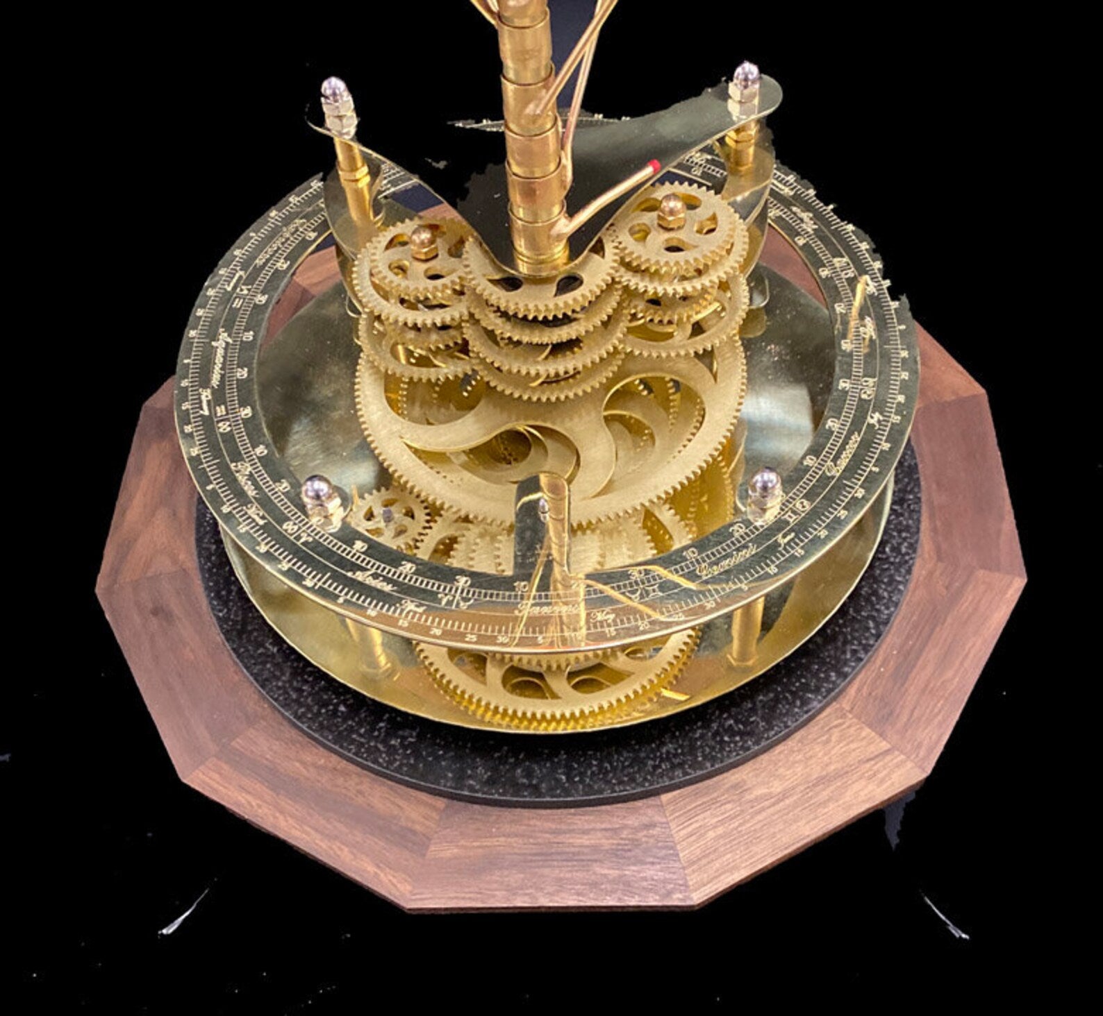 Close up photograph of Renaissance orrery depicting the solid brass gearwork of the orrery on a solid walnut base. A brass engraved calendar ring sits above the brass gearwork.