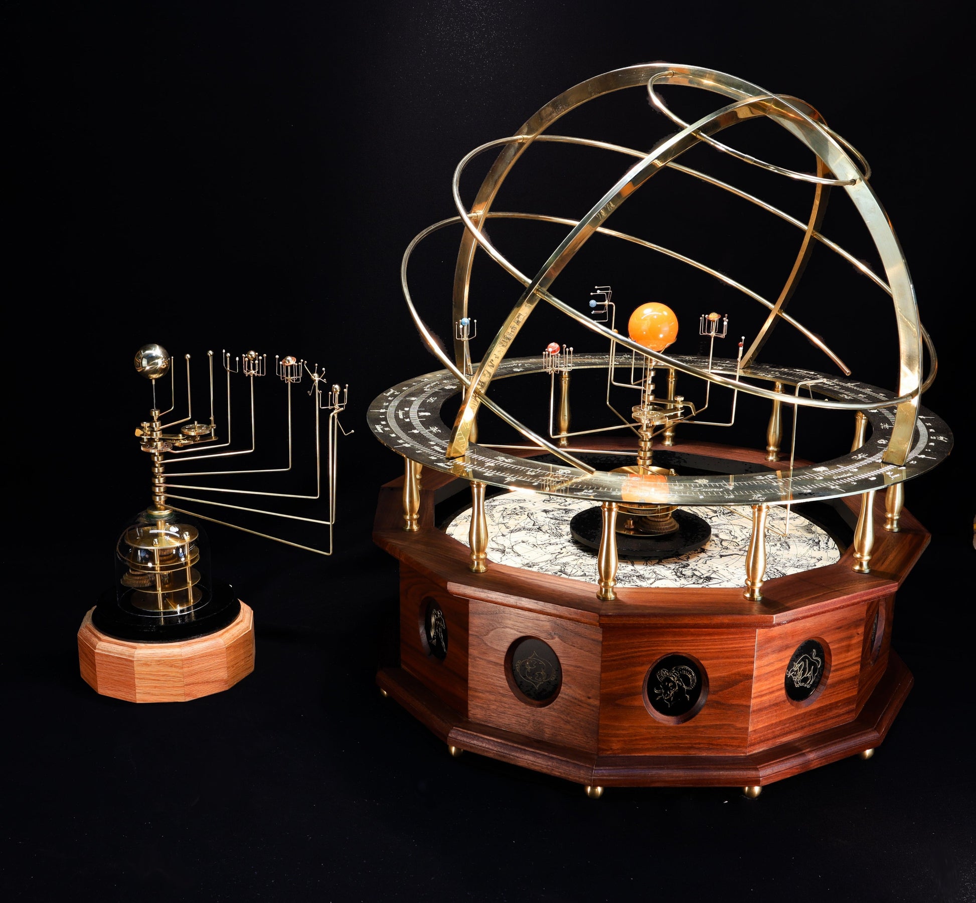 A premium museum, gallery quality, grand orrery with a solid brass calendar ring, brass planets and moons, and a half armillary sphere on top, all mounted on a hand-oiled black walnut wood base. Twelve panel depict each sign of the zodiac. Also pictured is the Wanderers Orrery with a solid brass sun and hematite planet set.