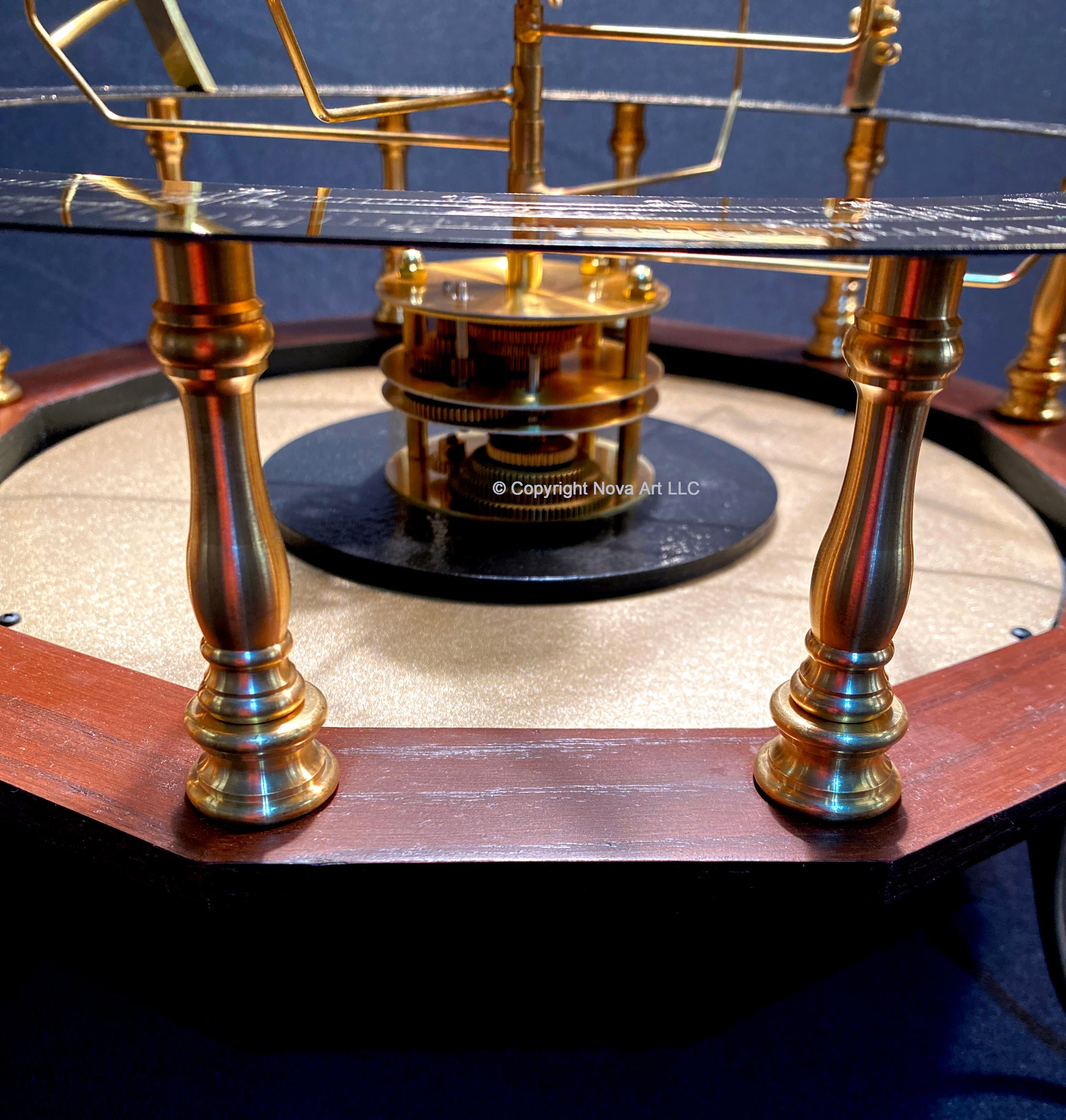 Close up of baby grand orrery from scienceart. Shows brass spindles and red mahogany base. Gear mechanism in middle of platen drives the orrery